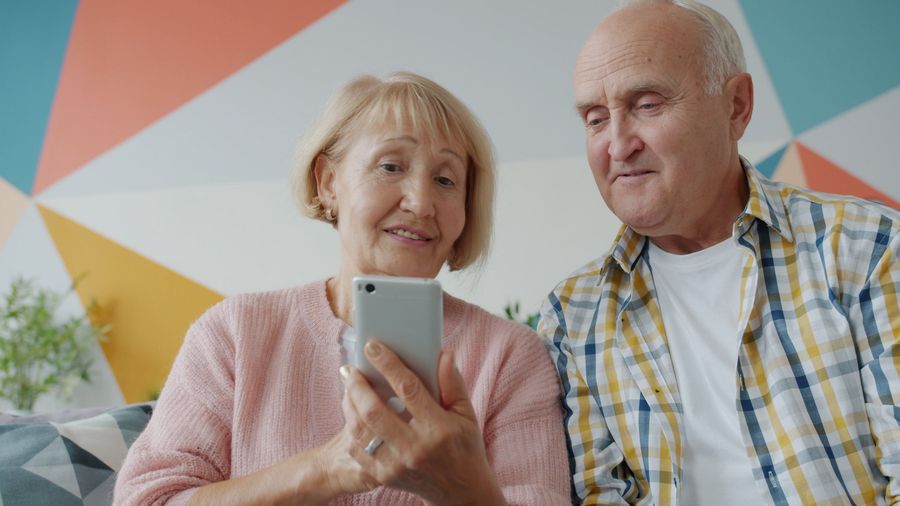 An older couple at home, smiling as they look at a phone together